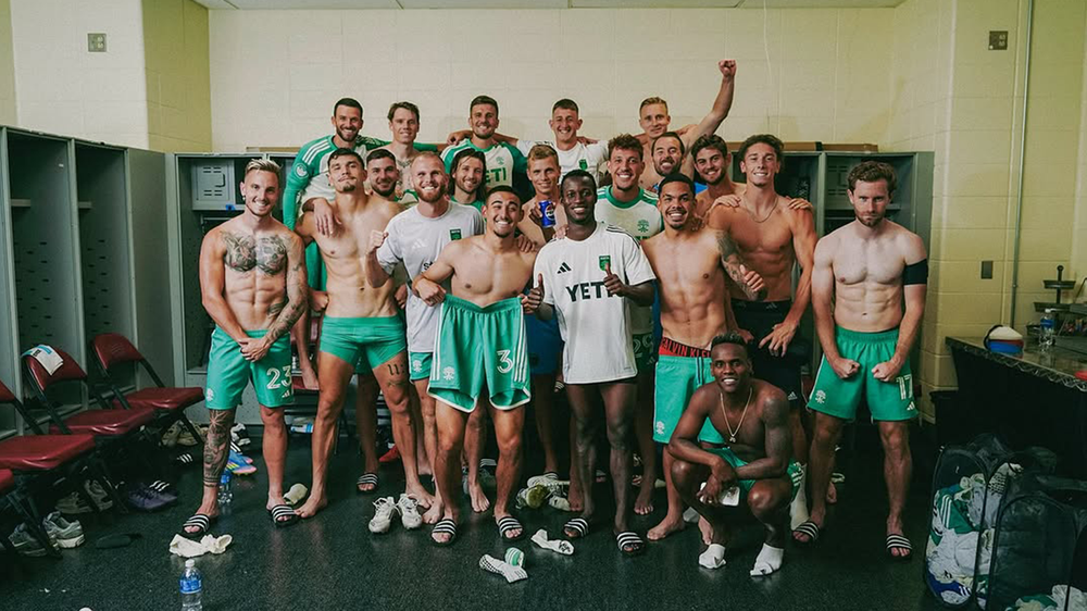 Austin FC players, some shirtless, celebrating in Colorado Rapids visitors' locker room after a win