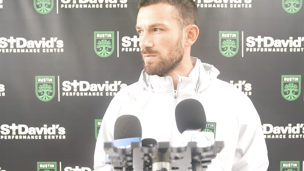 Brendan Hines-Ike standing with microphones in front of him at a press conference
