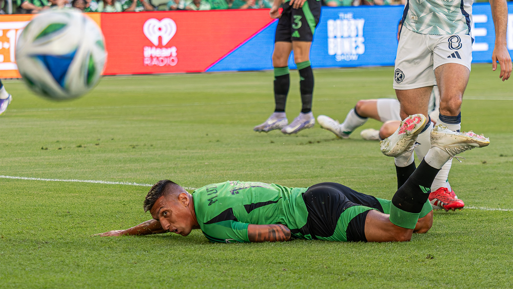 Myrto Uzuni lying on field watching ball move past him