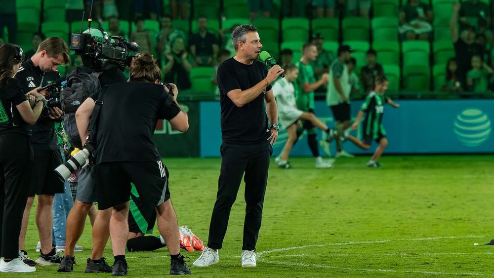 Nico Estévez with microphone and camera crew behind him, addressing Austin FC fans following win over LAFC