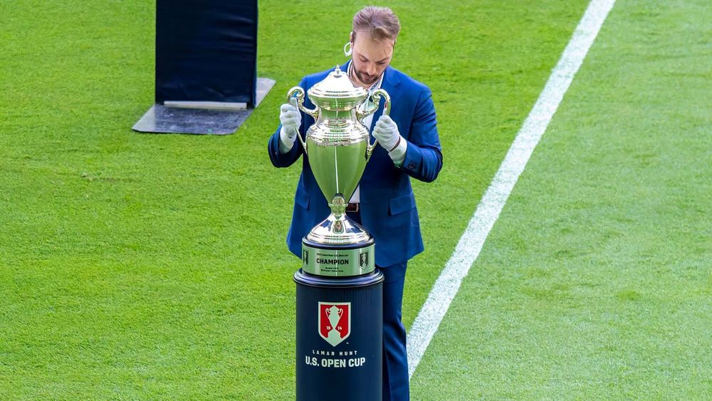 Official in suit wearing gloves putting U.S. Open Cup trophy on branded stand