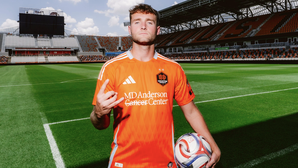Houston Dynamo FC forward Duncan McGuire standing with soccer ball in front of what's likely a greenscreen image of Shell Energy Stadium because the lighting is inconsistent