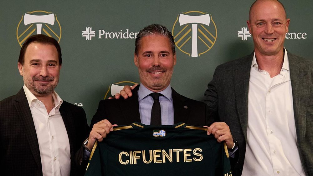New Portland Timbers FC head coach Martí Cifuentes flanked by club officials and holding up a jersey 