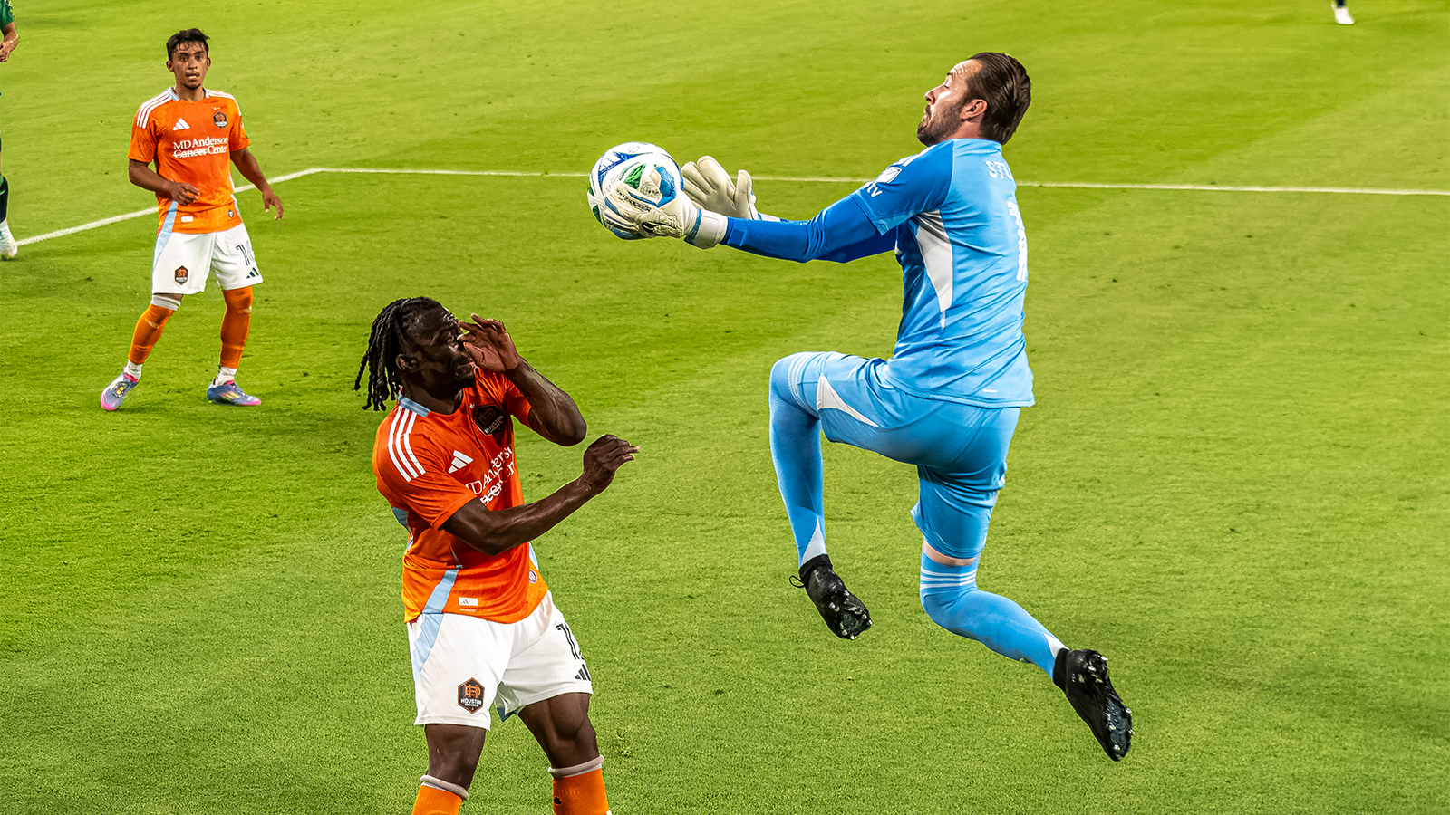 Brad Stuver leaping and catching ball in front of Houston Dynamo player