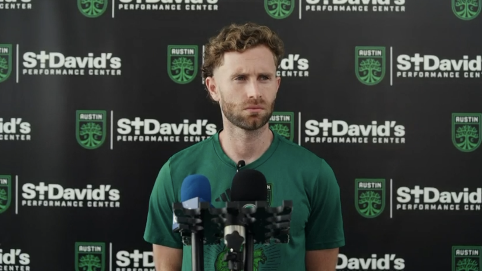 Jon Gallagher standing in front of microphones at press conference