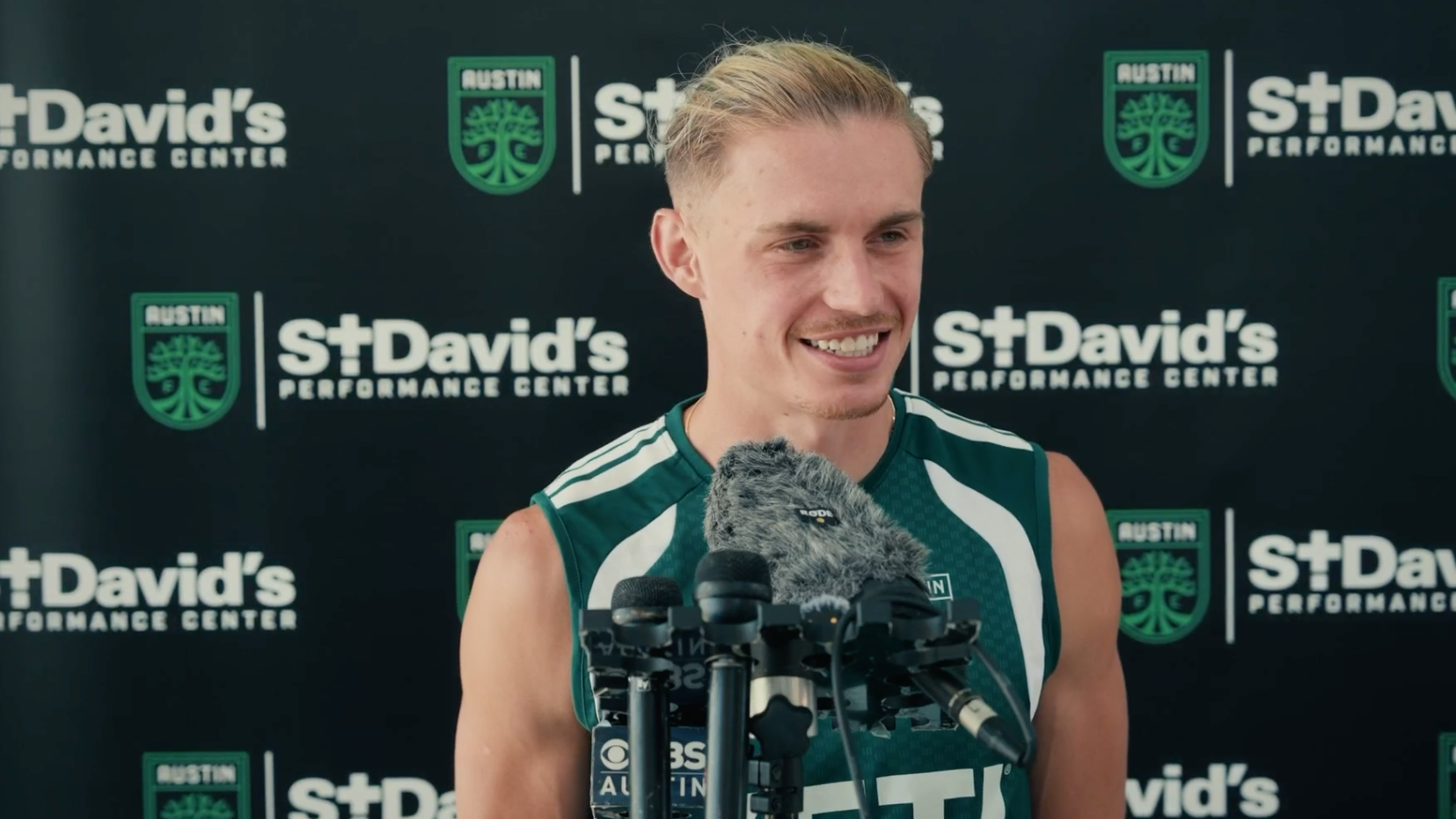 Austin FC's Przemysław Płacheta after training smiling, with microphones in front of him