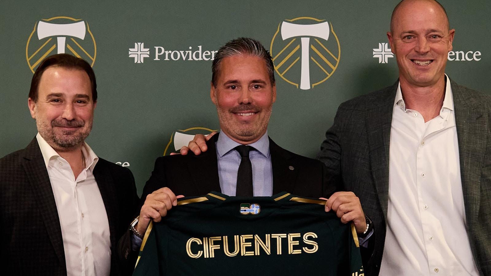 New Portland Timbers FC head coach Martí Cifuentes flanked by club officials and holding up a jersey 