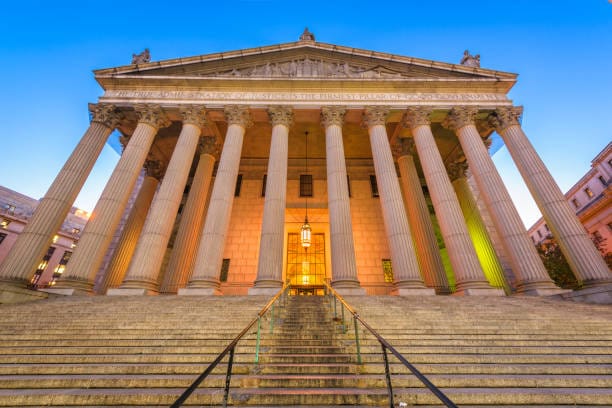 A photo of the New York County Courthouse, taken from the bottom of the steps. The courthouse has a columned entrance and is Greco-Roman in style. The image is from: 