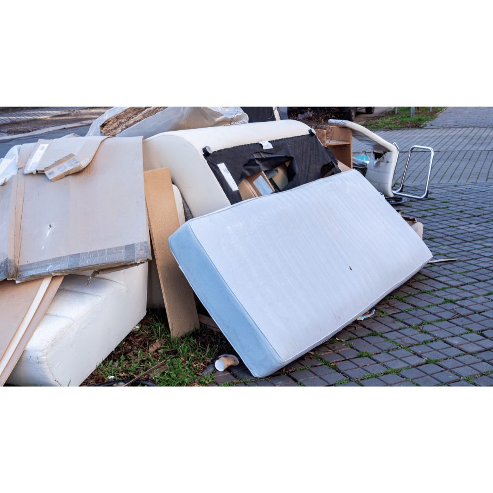 Old mattress and broken furniture awaiting removal on sidewalk