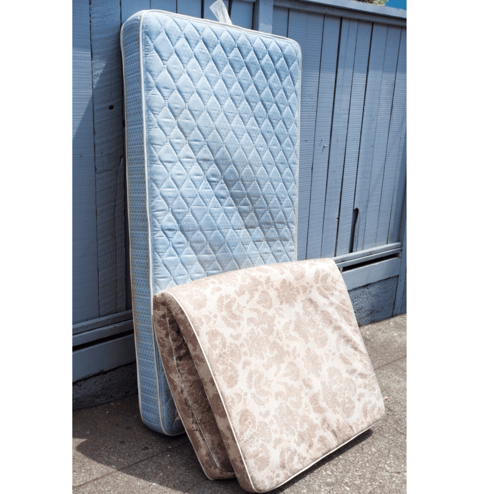 Two old mattresses leaning against a fence for recycling or disposal