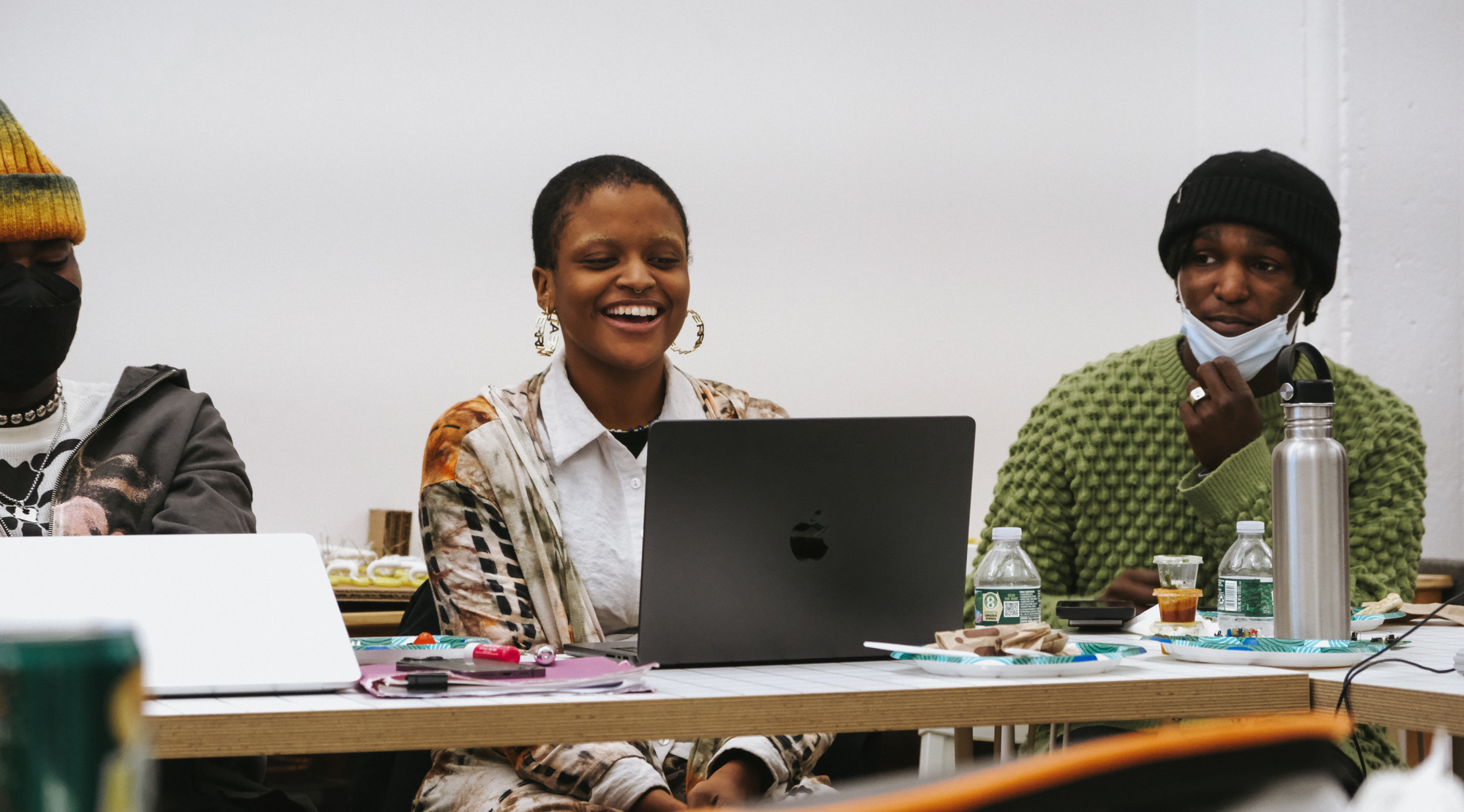 Readymag blog: Several people sitting around a worktable; the person in the center smiles at their laptop while others watch and talk, surrounded by markers, water bottles, papers, and other materials.
