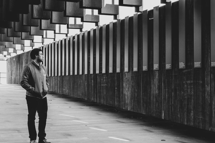Photo of Vaughn Hunt with medium curly hair in a green jacket and black jeans at The National Memorial for Peace and Justice.