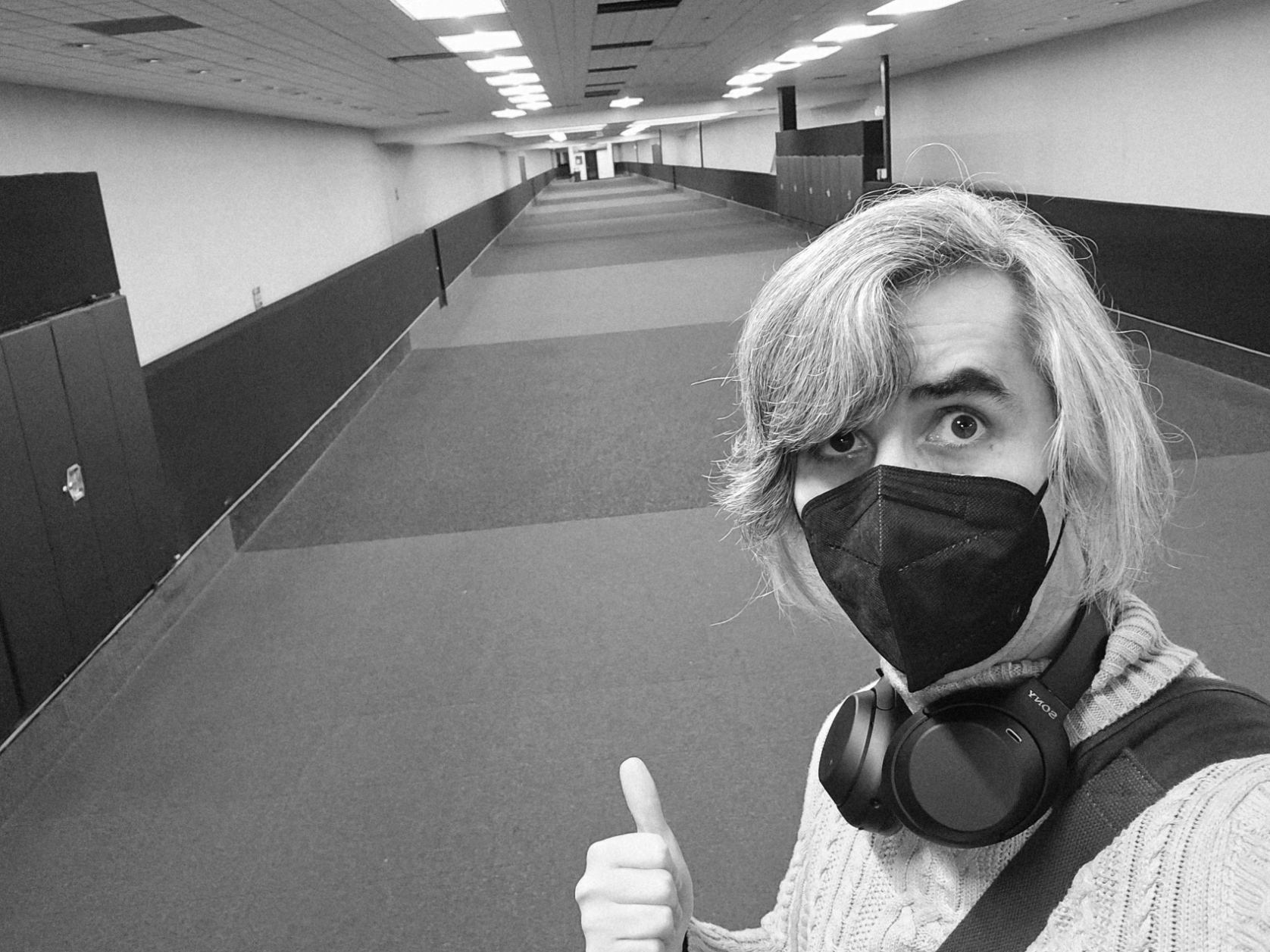 A selfie of me in a long tunnel. I'm wearing a turtleneck sweater, a face mask, and over-ear headphones around my neck. I'm pointing my thumb back at the tunnel, and have an apprehensive look on my face. The tunnel is empty.