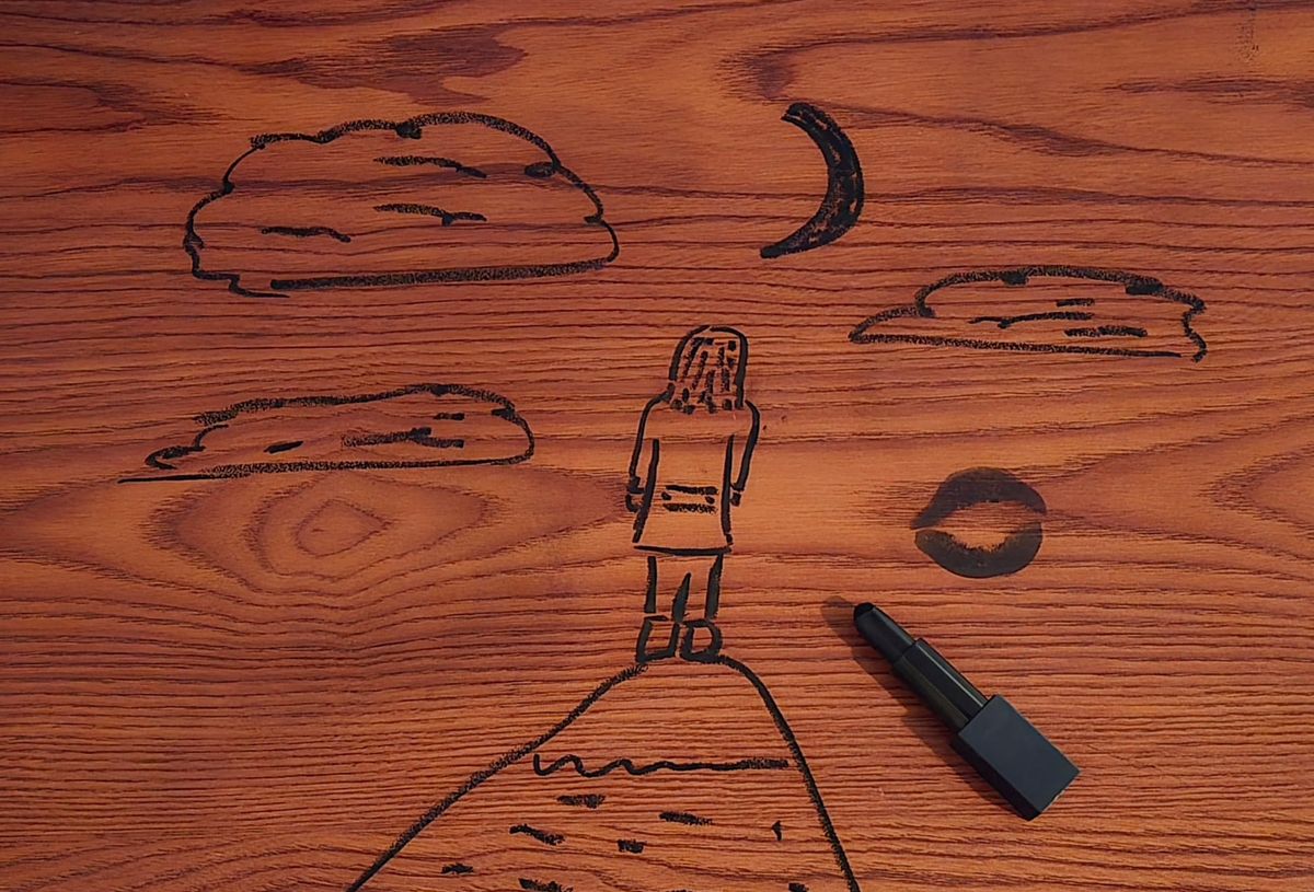 A drawing on wood of a person standing on a mountaintop, looking at a crescent moon and clouds. There is a black kissprint on the right, with an open tube of black lipstick sitting underneath