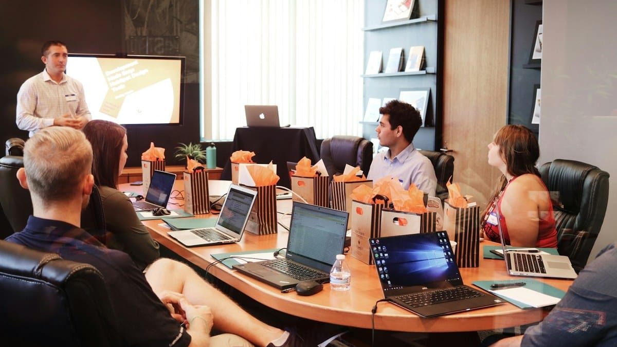 Bright conference room meeting around a wood table with laptops, no text overlay