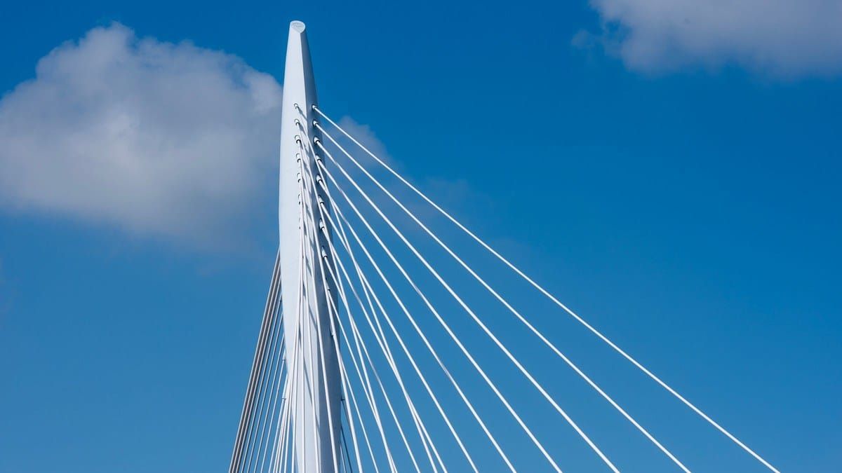 White cable-stayed bridge pylon with converging cables against a bright blue sky, no text overlay