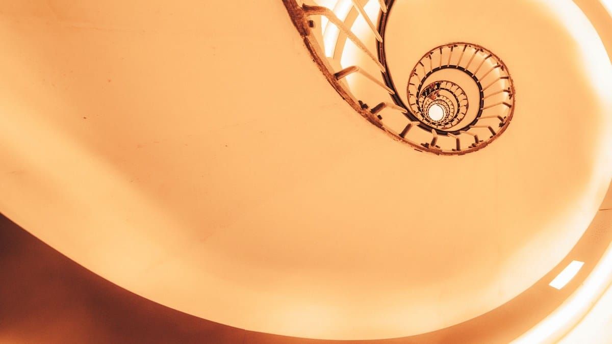 Looking up a spiral staircase in warm peach and coral light, modern architecture, no text overlay