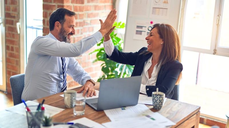 Two colleagues high-fiving at a bright office desk after a successful B2B outreach win
