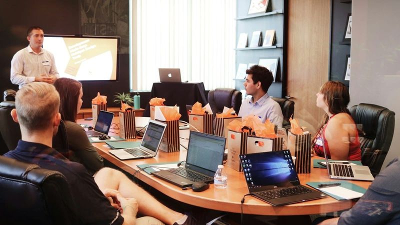 Bright conference room meeting around a wood table with laptops, no text overlay