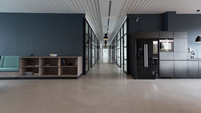 Modern office corridor with glass meeting rooms, navy wall, and black pendant lights