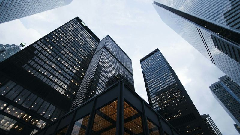 Looking up at dark glass skyscrapers against a pale sky, no text overlay