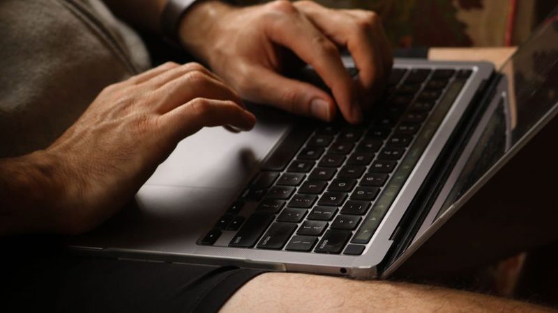 Close-up of hands typing on a silver laptop resting on a lap in warm, low evening light; no text overlay