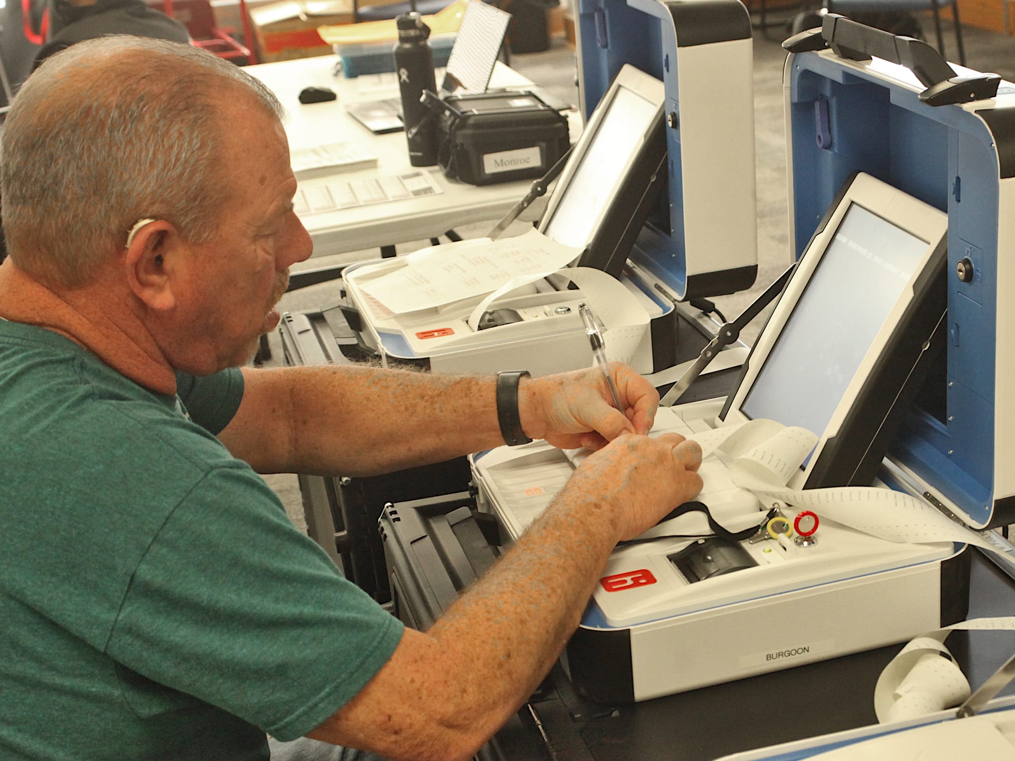 man seated at voting machine clipping paper tape together