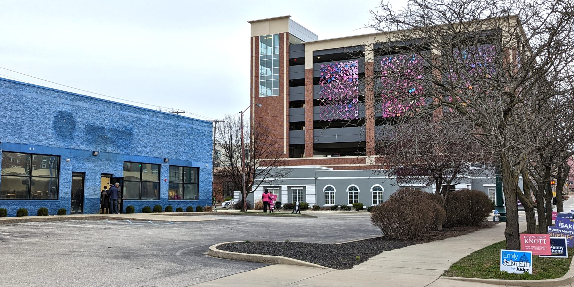 view of blue building on the left parking lot in foreground and parking garage with colorful tiles in the background to the right