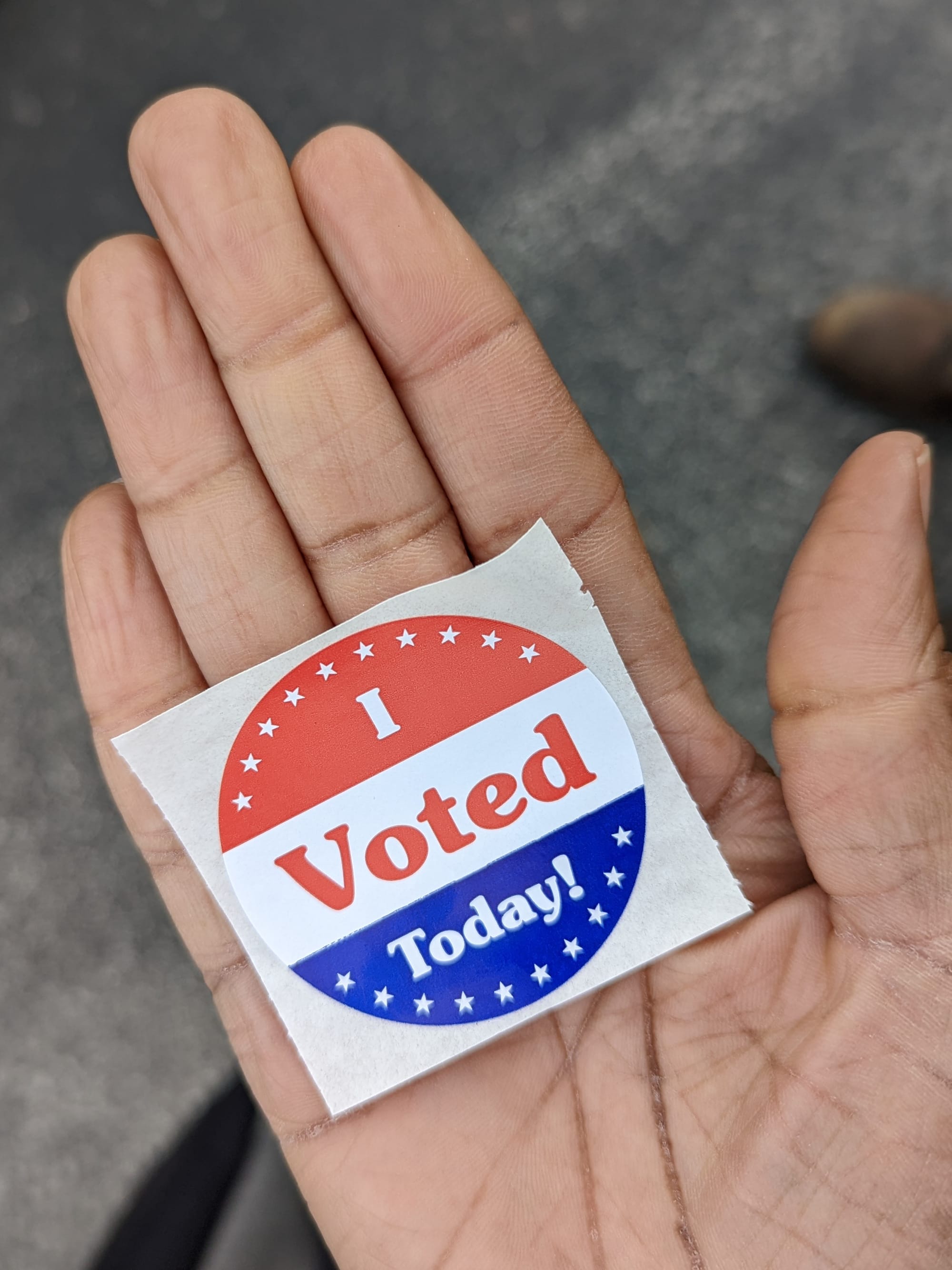 a palm-up flat hand on which an "I Voted" sticker is lying