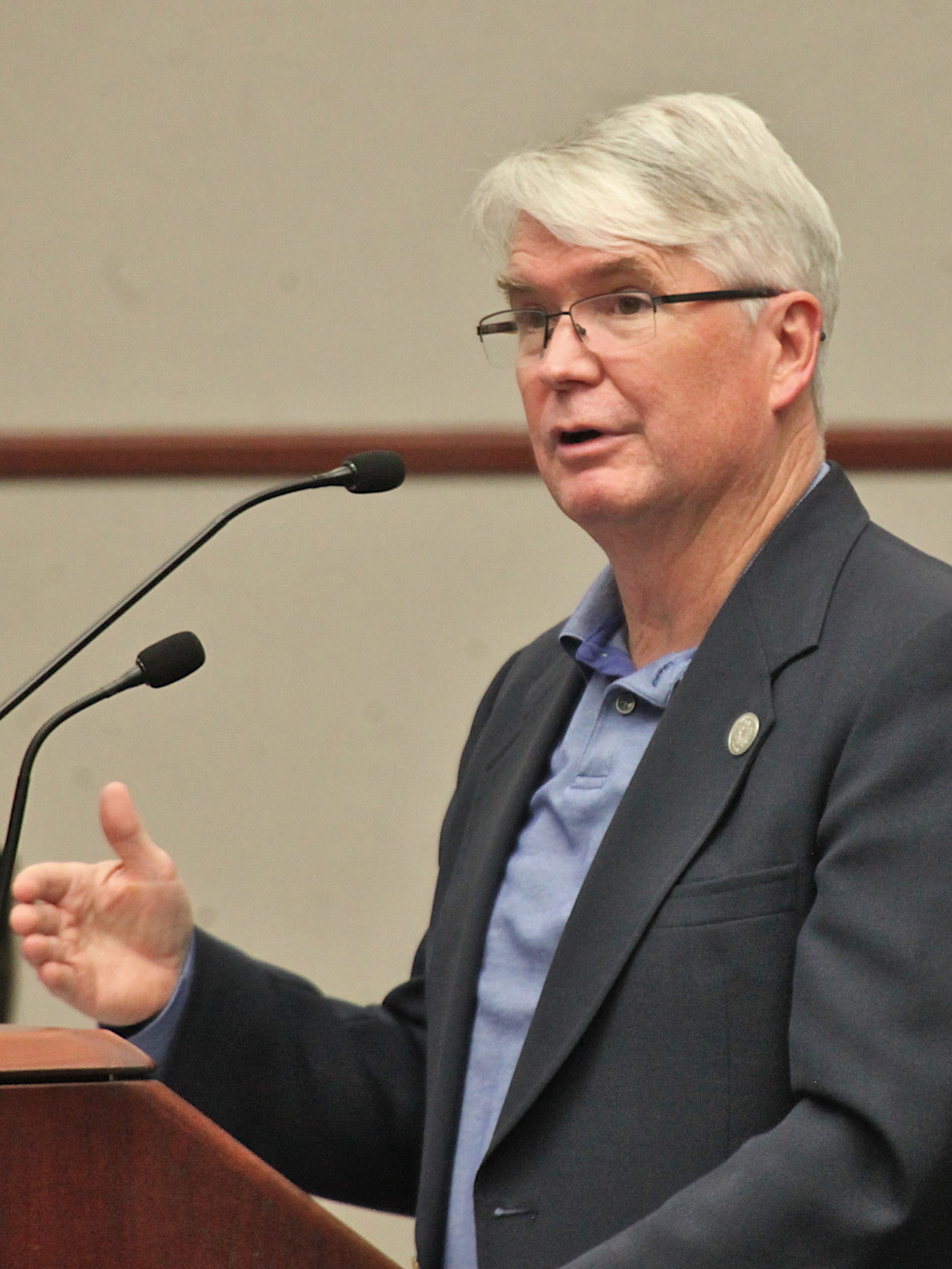 man standing at a podium and mic talking, gesturing with right hand