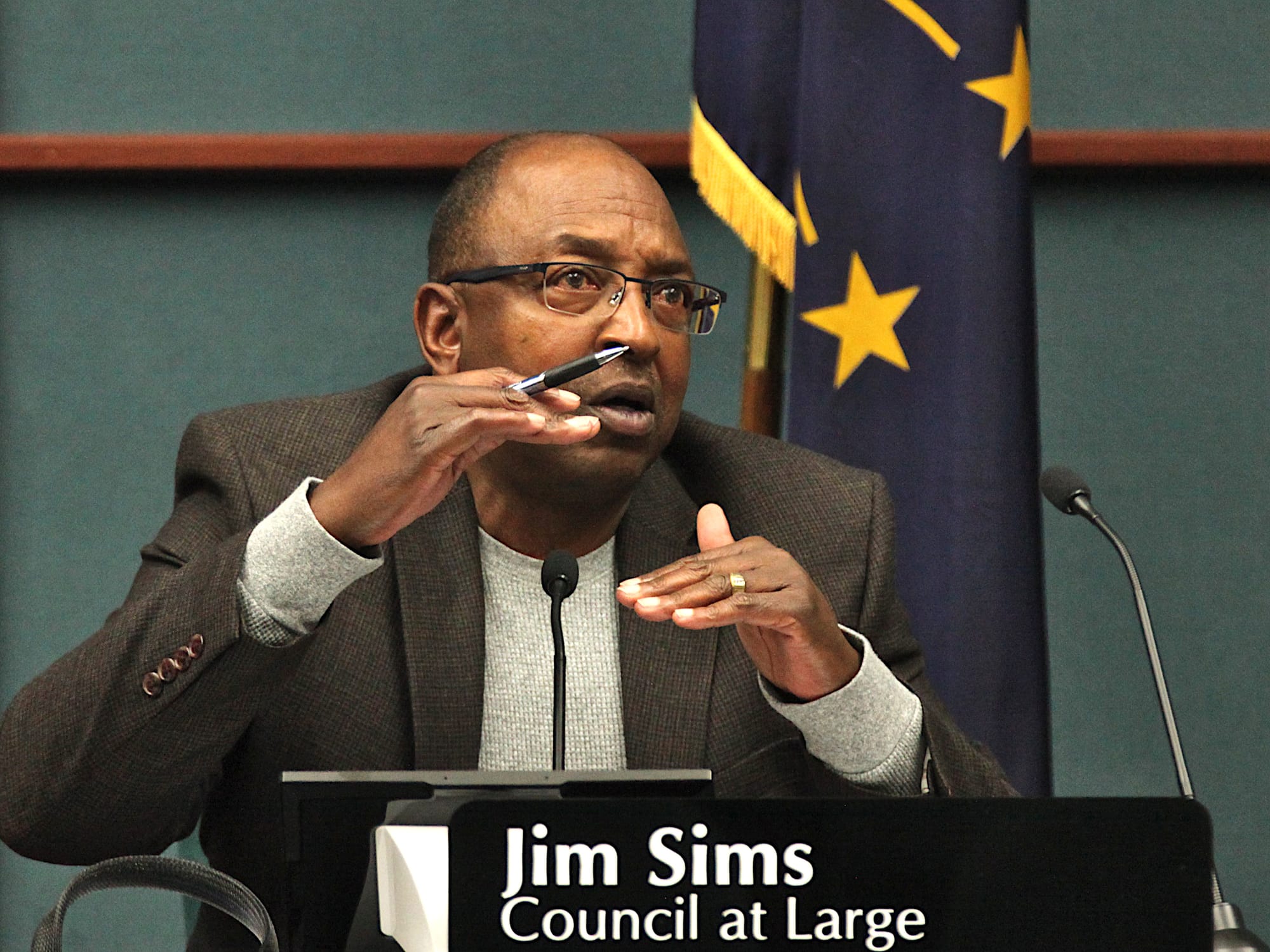man sitting at city council table with name plate mic holding his hands flat a certain distance apart vertically