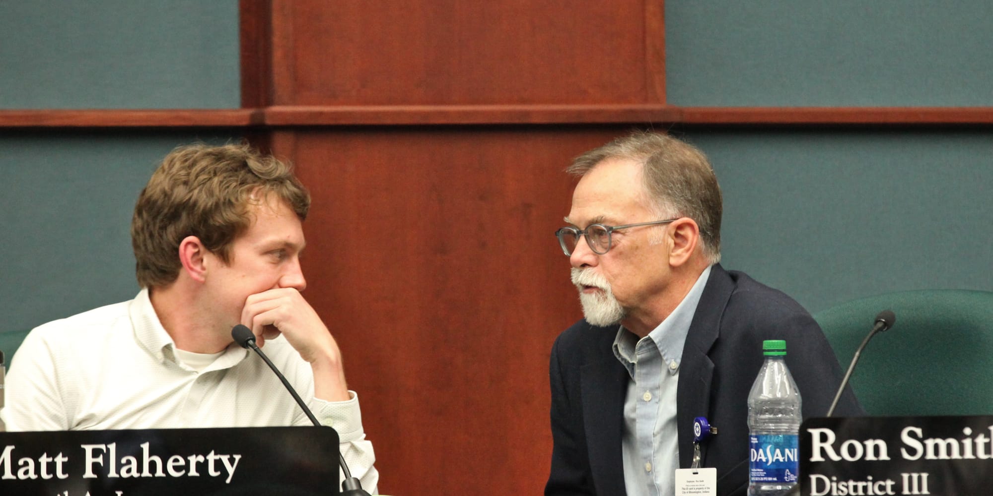 two men seated talking at city council dais