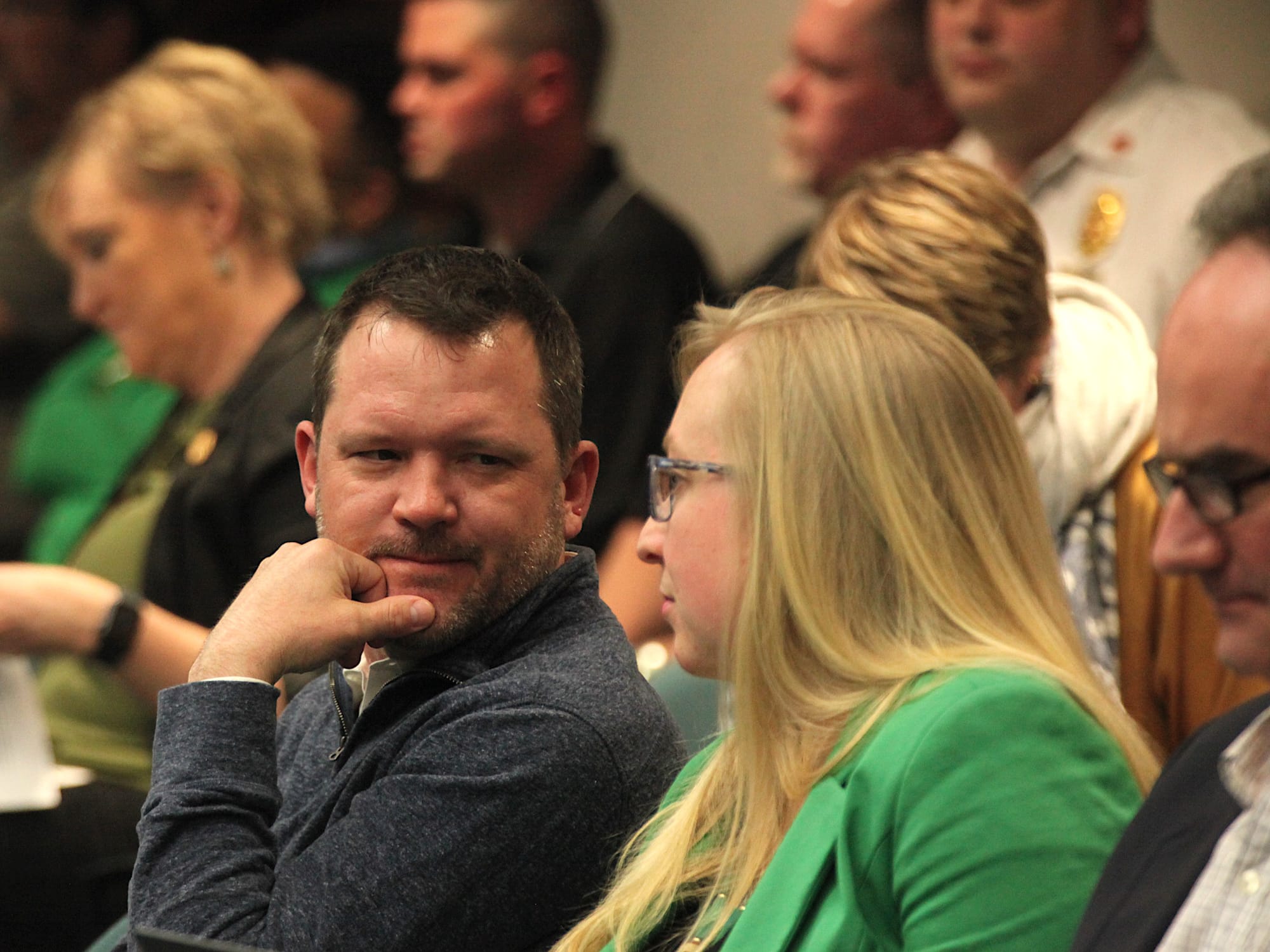 man with hand supporting chin looking at a woman sitting to his left as he sits in a chair