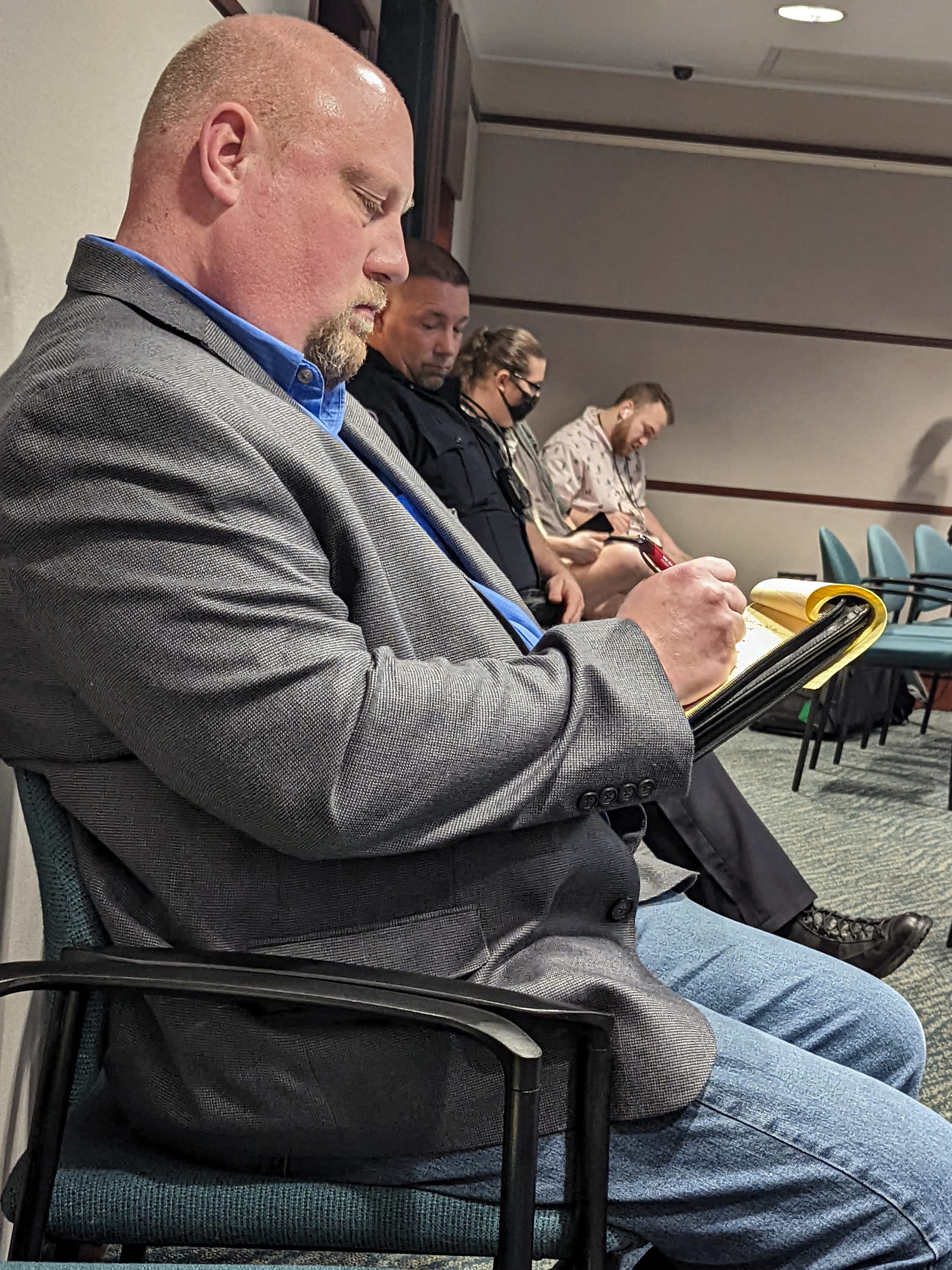 man seated facing to the right, taking notes on a pad