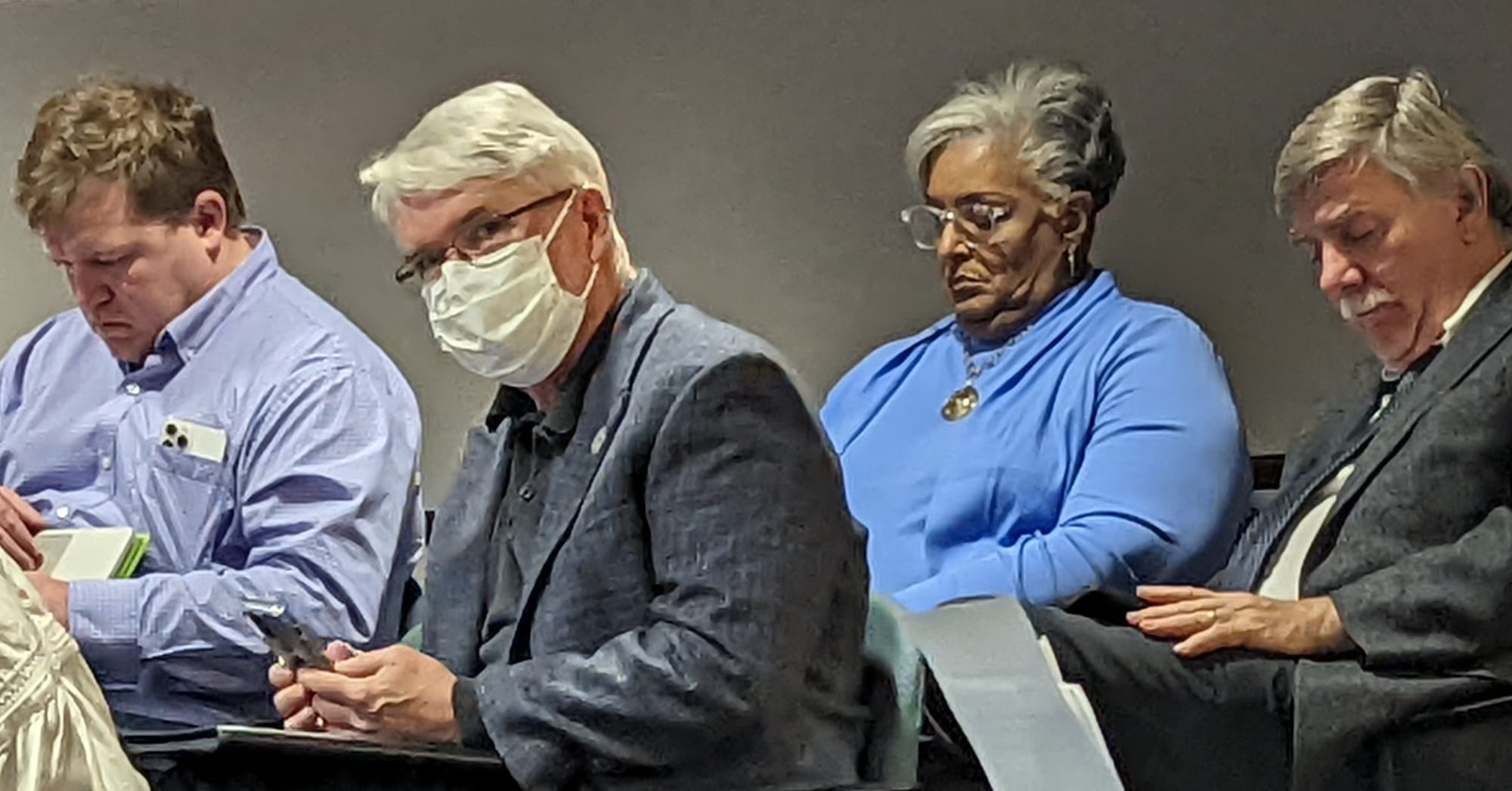 four people sitting in chairs in the city council chambers