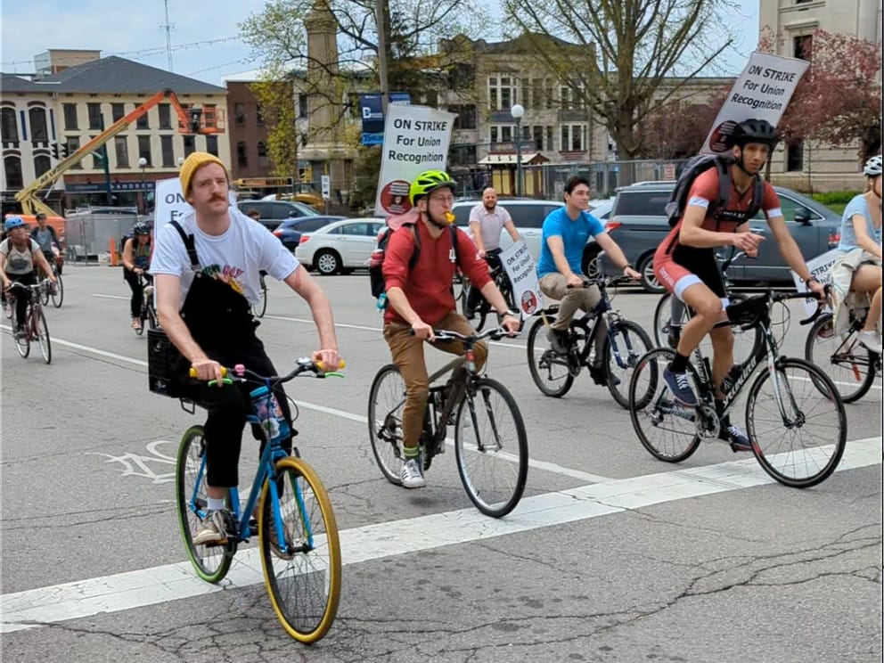 bicyclists riding from left to ride with signs that read "ON STRIKE for union recognition"