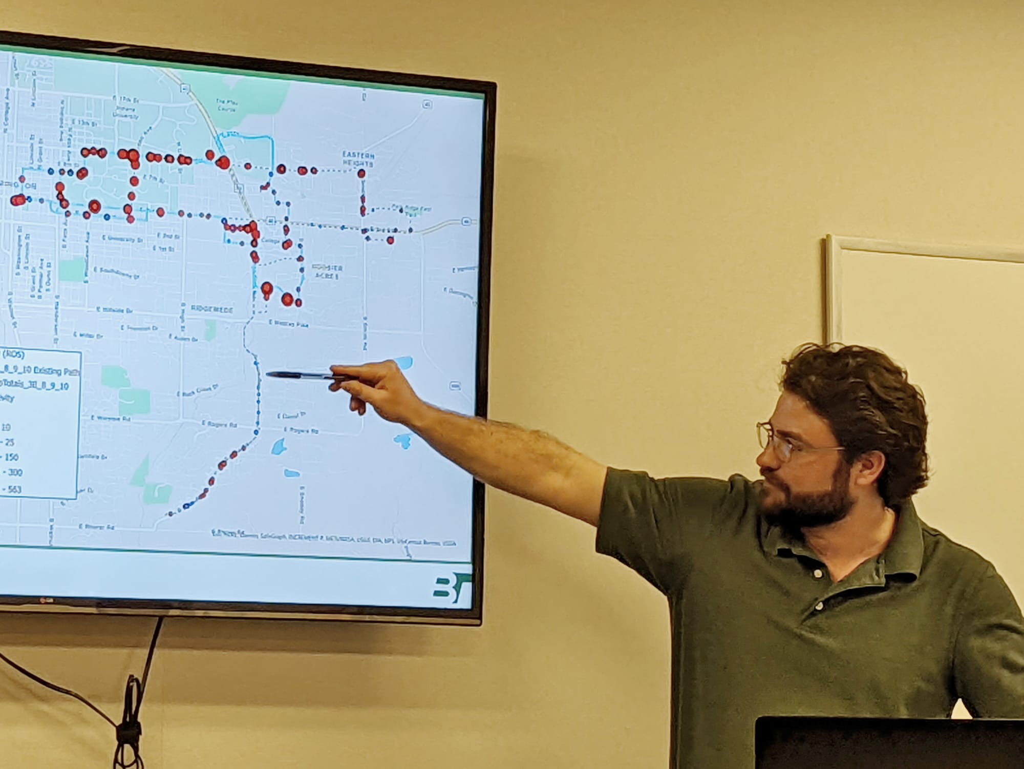 man stqnding at big screen pointing at a bus route depicted there