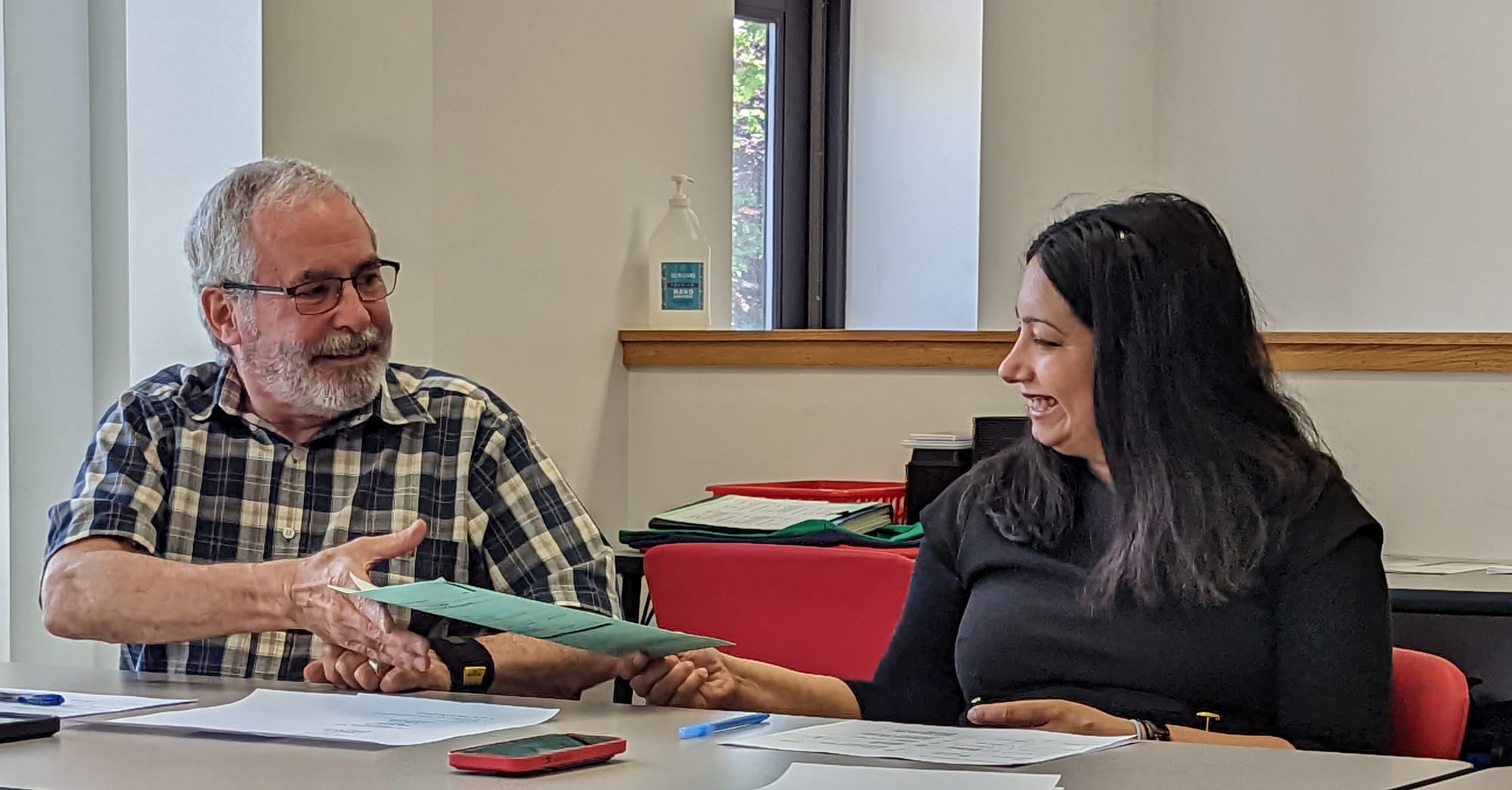 From left: maan accepting a piece of paper from woman who is seated to the right of the frame (the man's left)