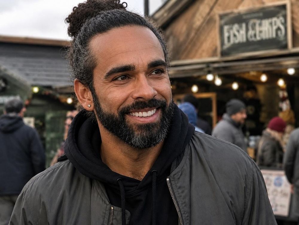 Smiling bearded man in olive jacket at an outdoor market beneath a Fish and Chips sign