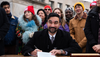 Mamdani signs an executive order during a news conference at Grand Army Plaza with a row of supporters standing behind him