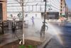 The light reflects a rainbow as kids play in a sprinkler on a corner near a construction site