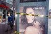 A man walks by a bus stop displaying a Chanel ad with caution tape wrapped across it