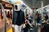 A man wearing a mask shaped like a computer over his head stands on a subway train