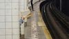 A hand holding a book is visible behind a subway platform column