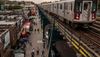 A train on an elevated subway line passes shops and pedestrians on Roosevelt Avenue in Corona, Queens