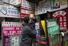 A man holding a baby outside of a storefront covered in signs written in multiple languages