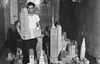 A man creates a miniature scale model of New York City, holding up one of the buildings