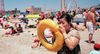 A woman blowing up a round yellow pool float on a crowded beach