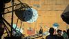 Shadows of people and infrastructure are cast upon a mural depicting a circus