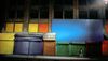 A man walks in front of a row of buildings with some windows boarded up with colorful boards and their doors painted a variety of bright colors